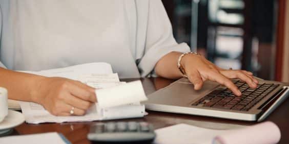 mão de mulher digitando no notebook fazendo cálculos para pagar boleto online